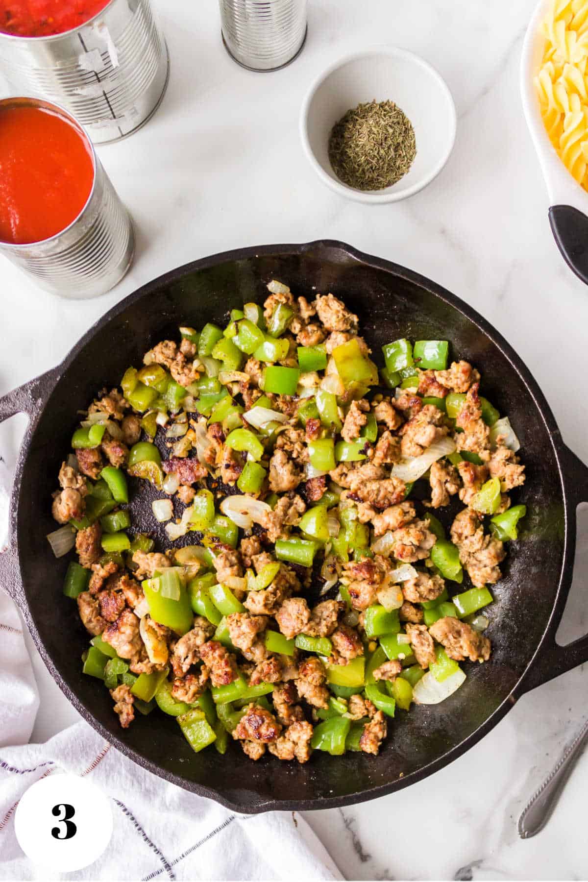 Diced green peppers and onions with Italian sausage in a skillet. 