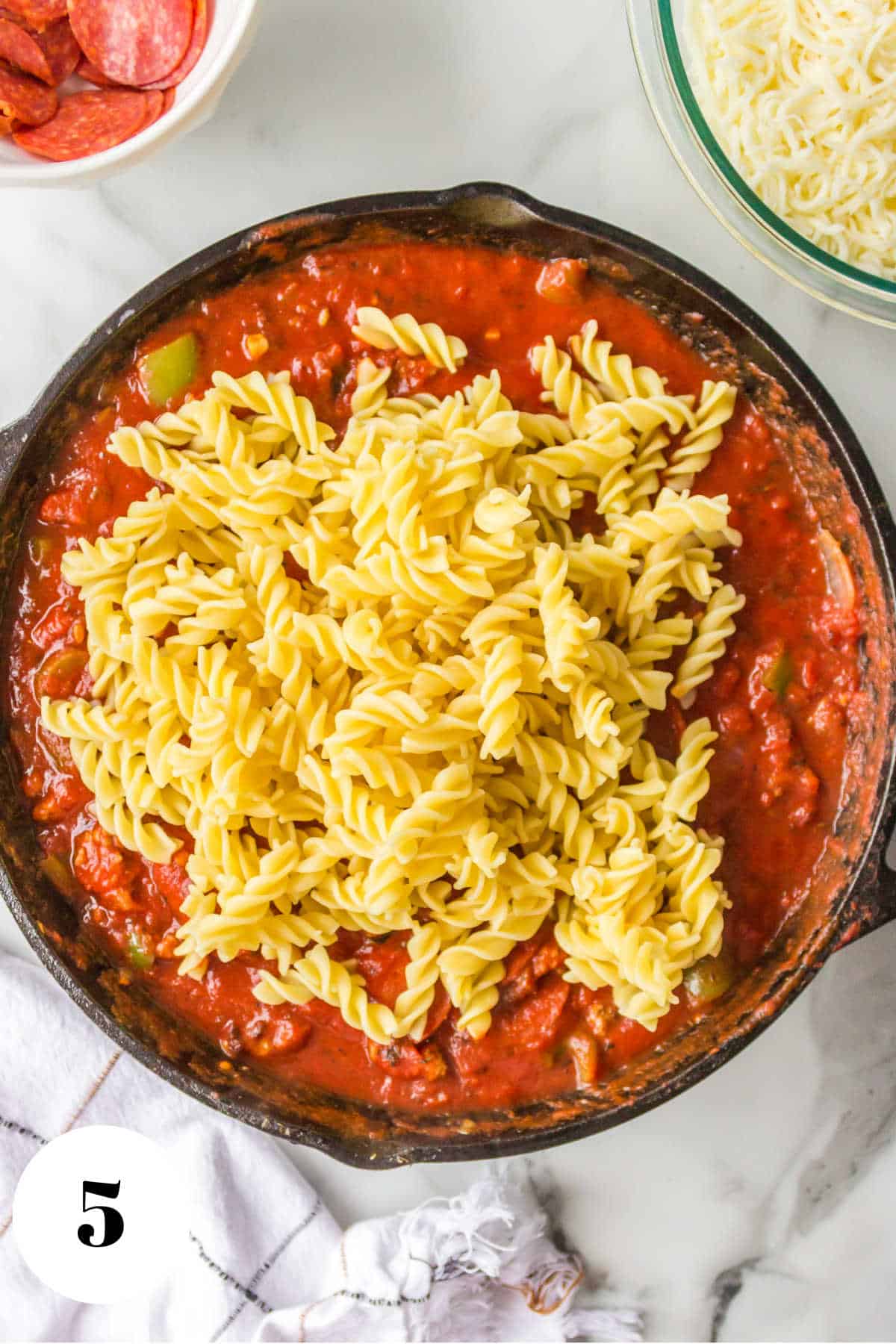 Cooked pasta on top of tomato sauce in a skillet.