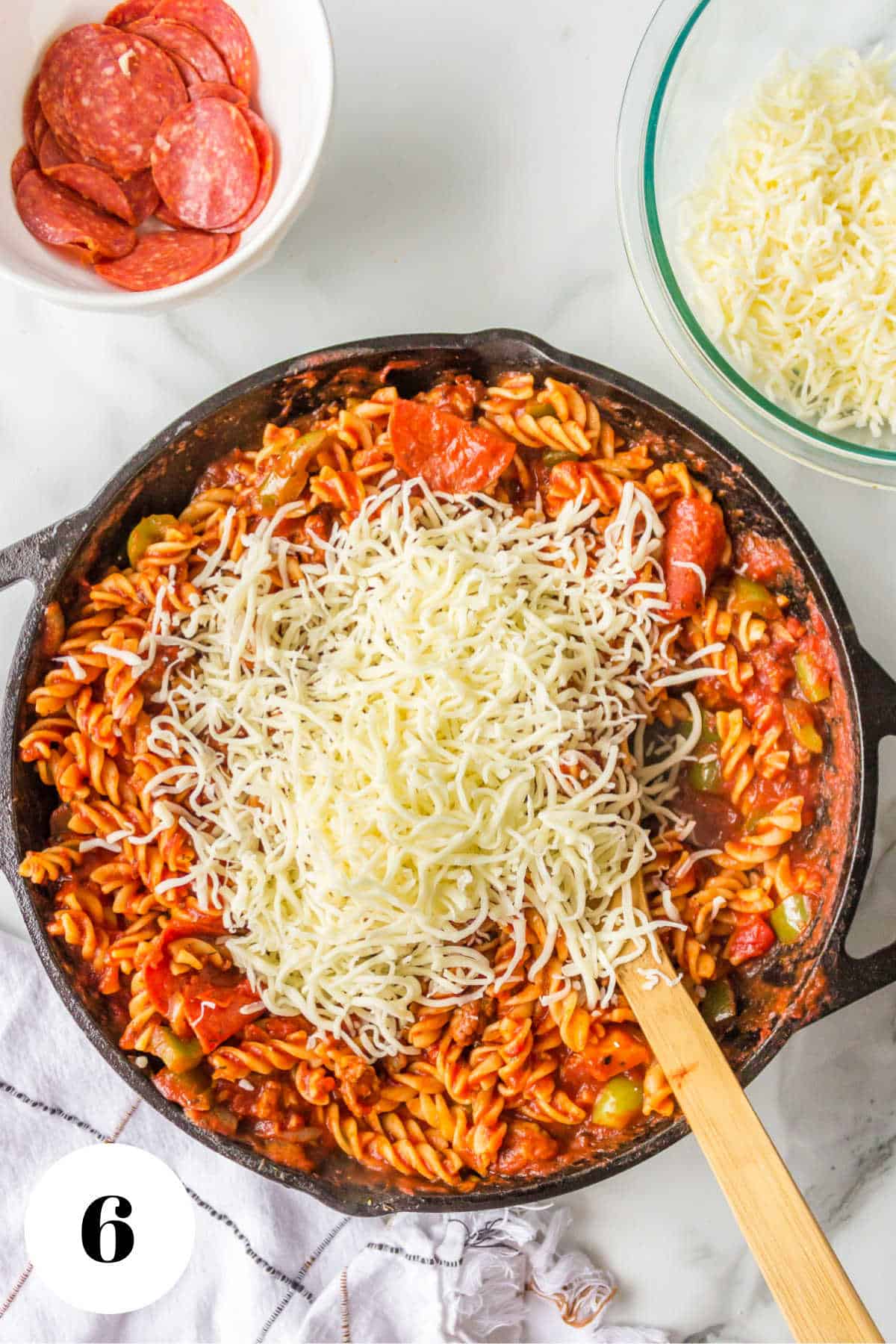 Shredded mozzarella cheese on top of pizza pasta in a skillet. 