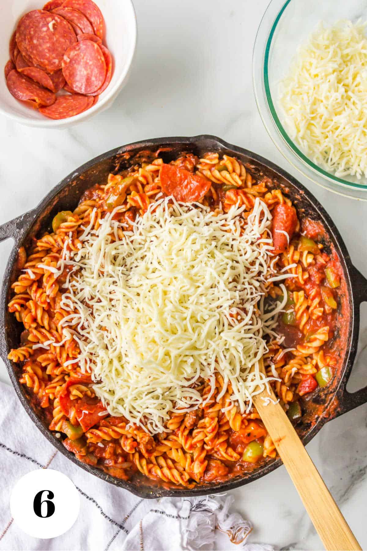 Shredded mozzarella cheese on top of pizza pasta in a skillet.