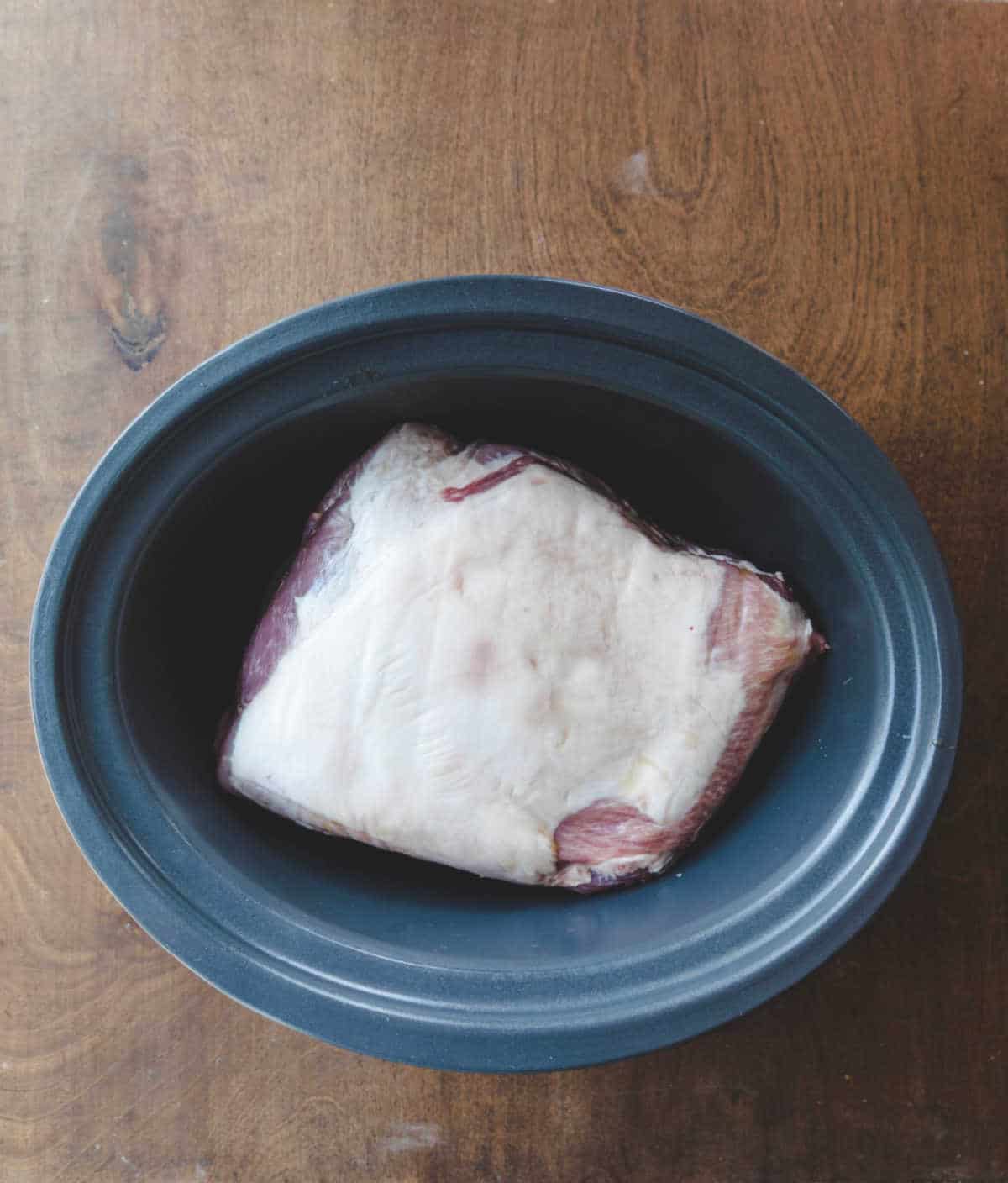 A pork roast in a slow cooker insert. 