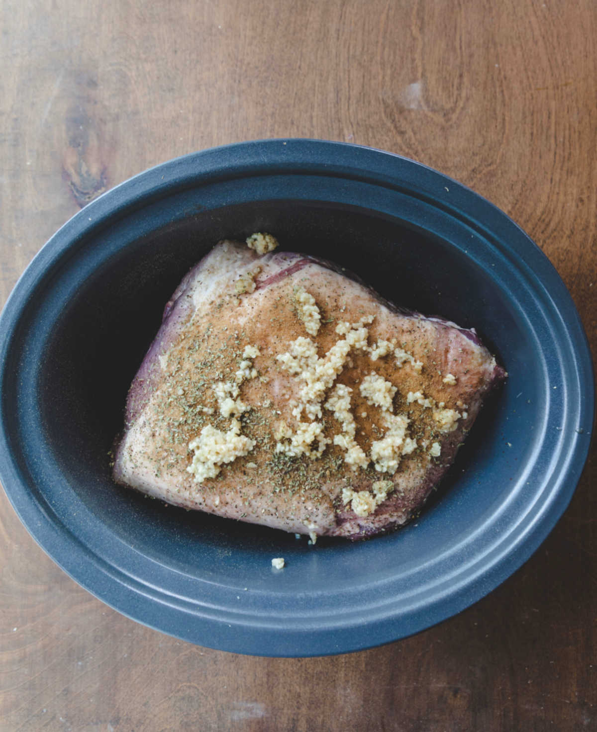 Uncooked pork roast in a slow cooker topped with minced garlic. 