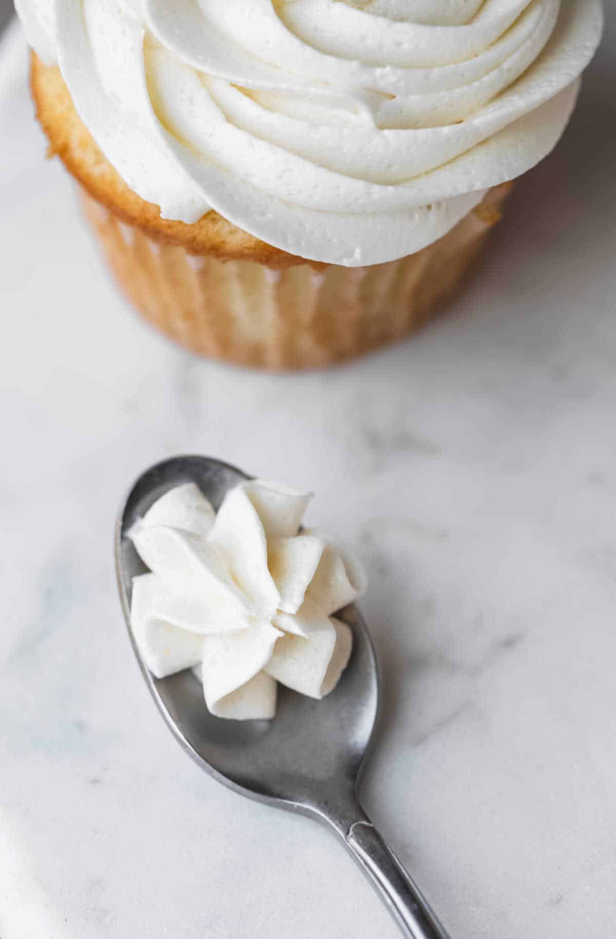 A spoon holding a small piped bit of vanilla buttercream frosting. 