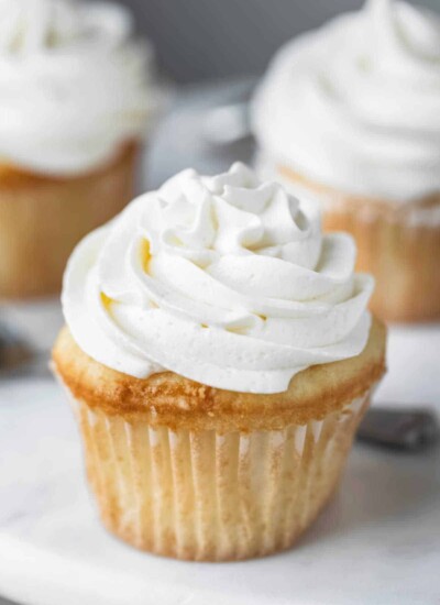White cupcake with a swirl of vanilla buttercream frosting on a marble cake stand.