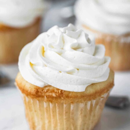 White cupcake with a swirl of vanilla buttercream frosting on a marble cake stand.