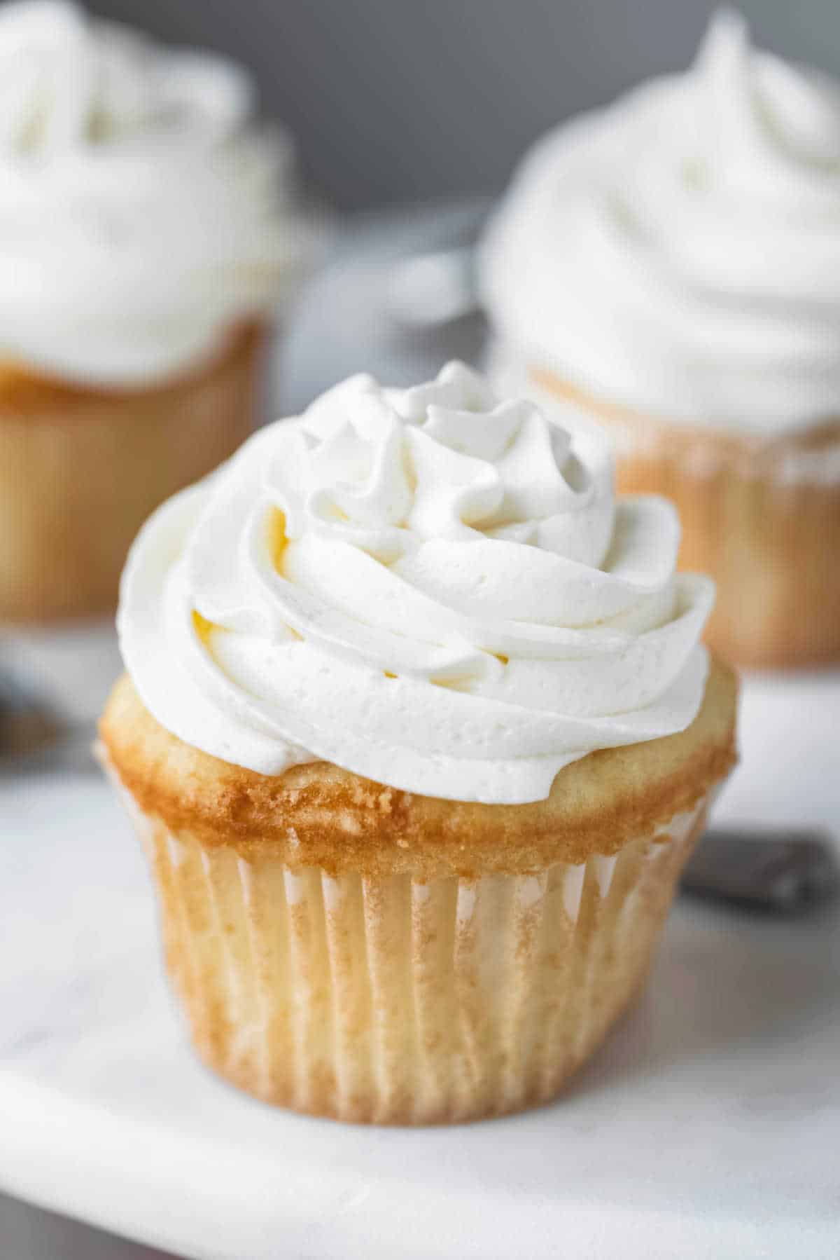 White cupcake with a swirl of vanilla buttercream frosting on a marble cake stand.