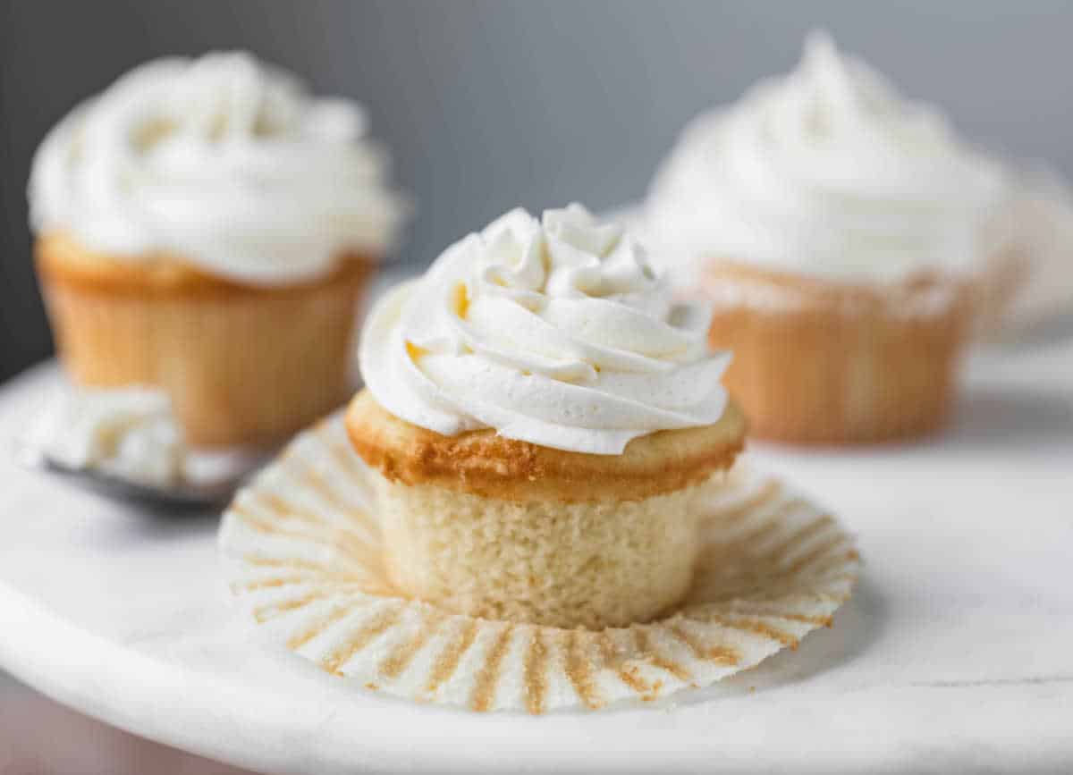 white cupcake with vanilla frosting with its wrapper pulled down.