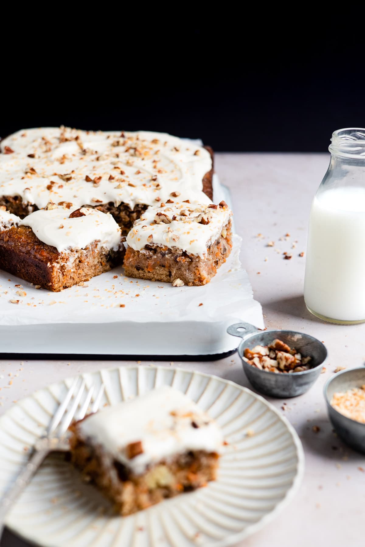A tray of carrot cake next to a glass of milk.