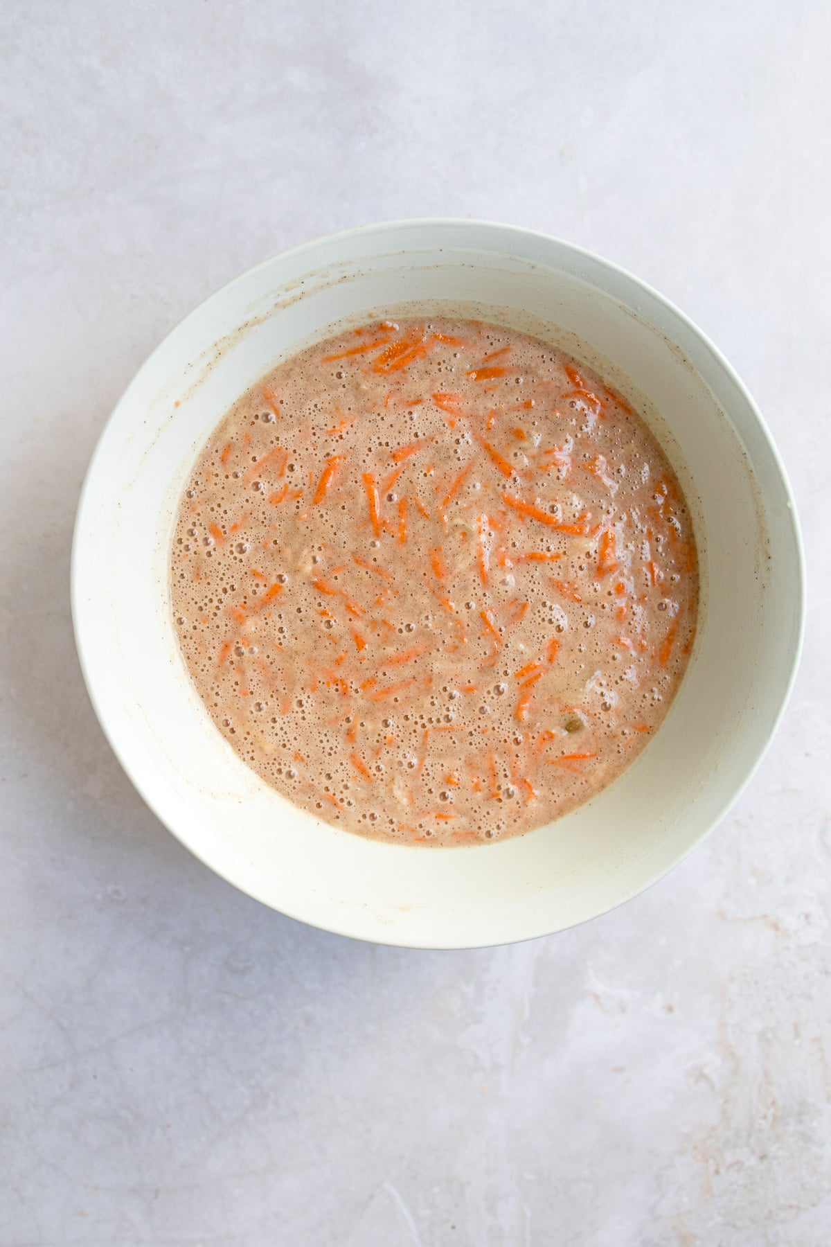 Wet and dry ingredients for carrot cake mixed together in a mixing bowl. 