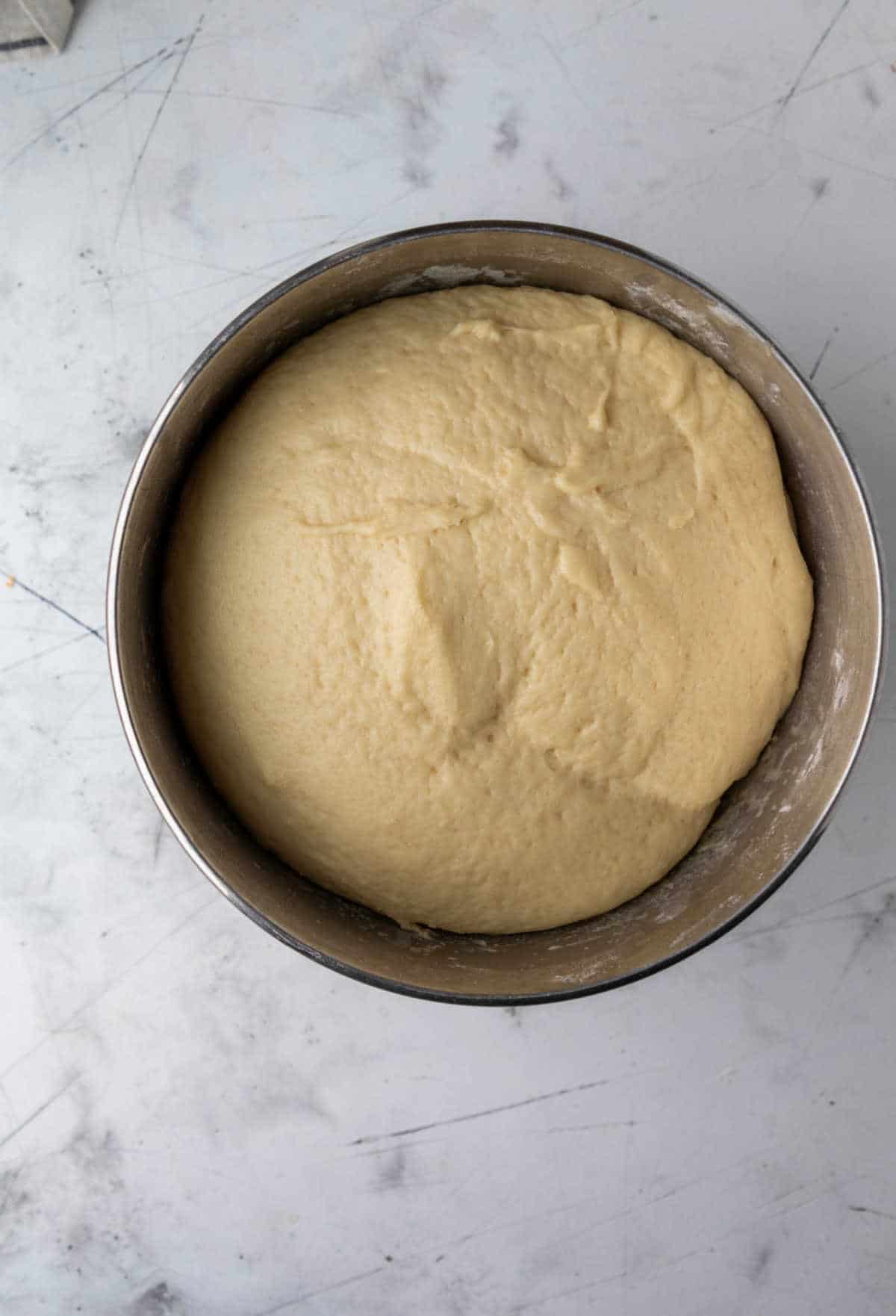 Risen Hawaiian sweet roll dough in a silver mixing bowl. 