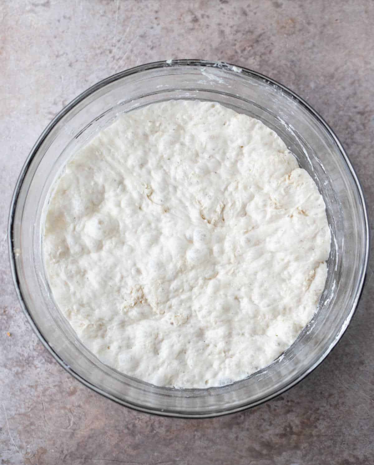 Risen no knead bread dough in a glass mixing bowl.