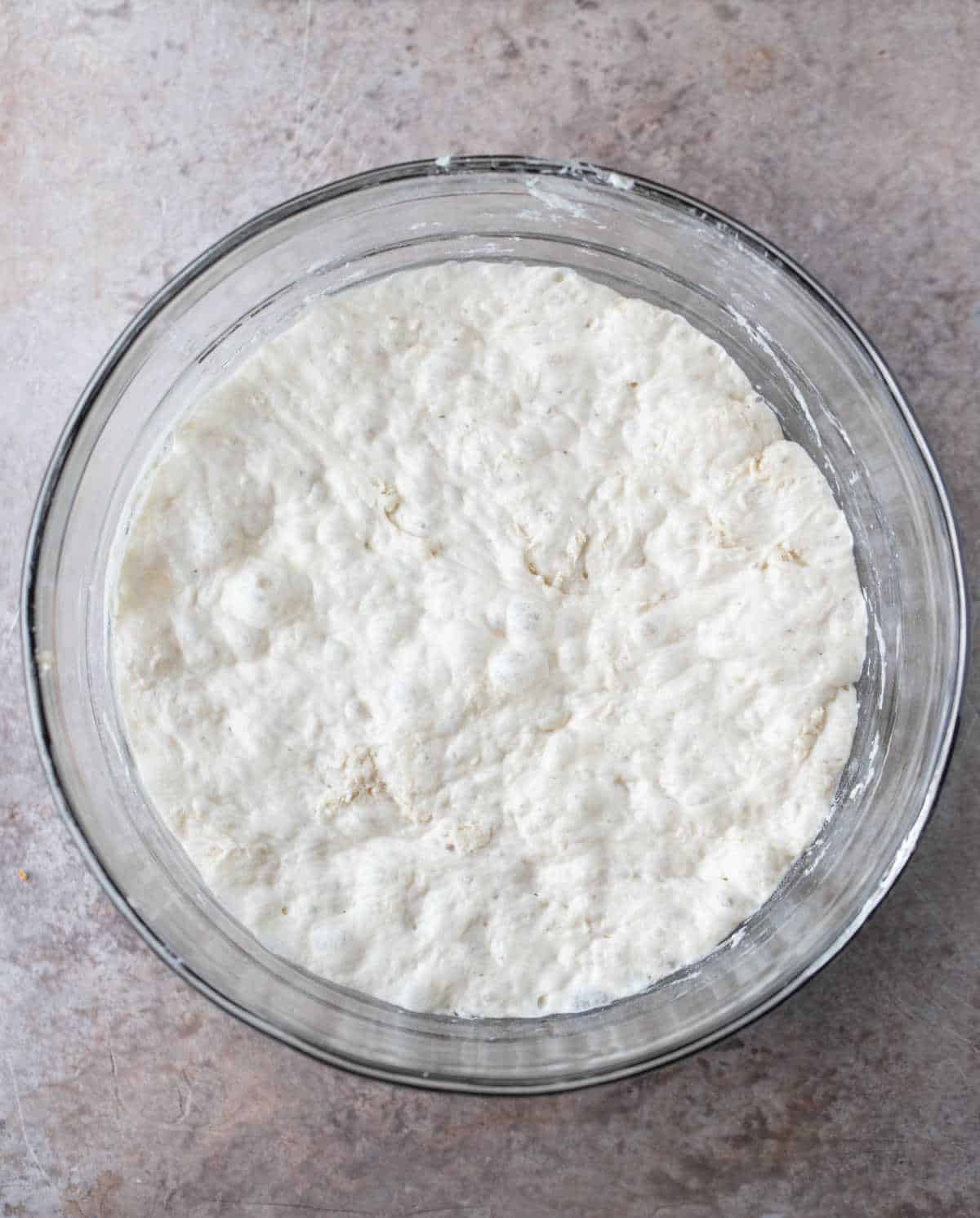 Risen no knead bread dough in a glass mixing bowl. 