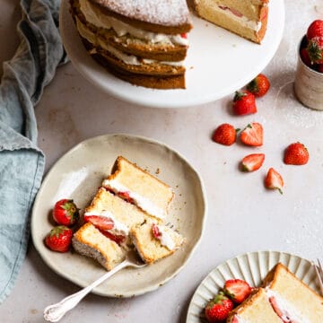 A slice of strawberry shortcake cake with a fork taking a bite next to the rest of the cake.