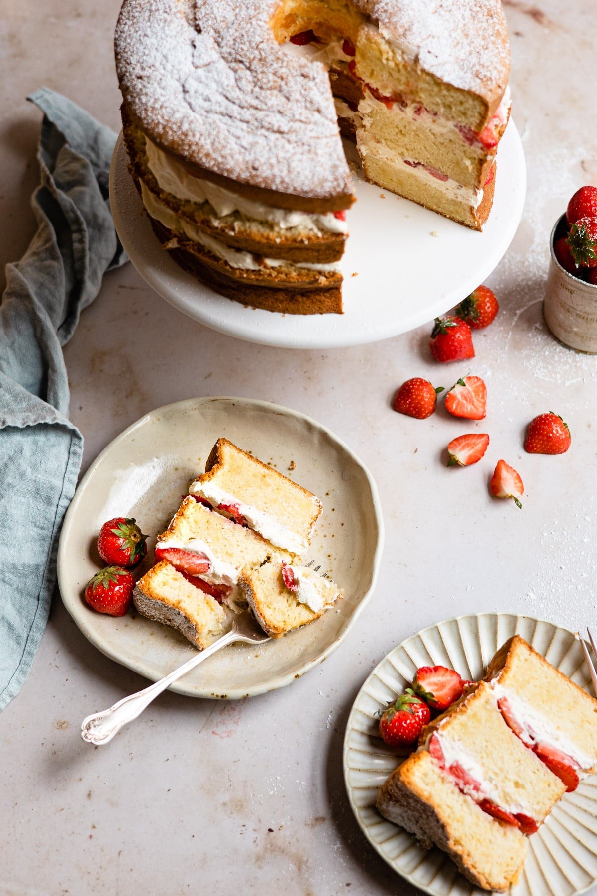 Two plates of strawberry shortcake cake next to a full cake. 