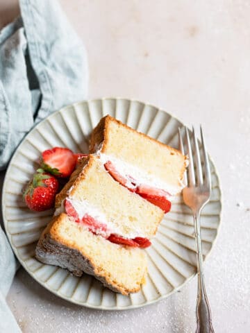 A piece of strawberry shortcake cake on a plate with strawberries and a fork.