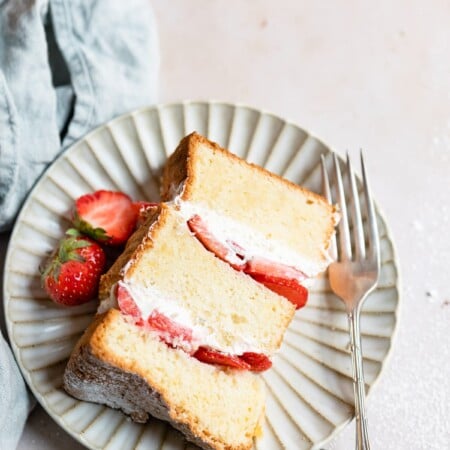 A piece of strawberry shortcake cake on a plate with strawberries and a fork.