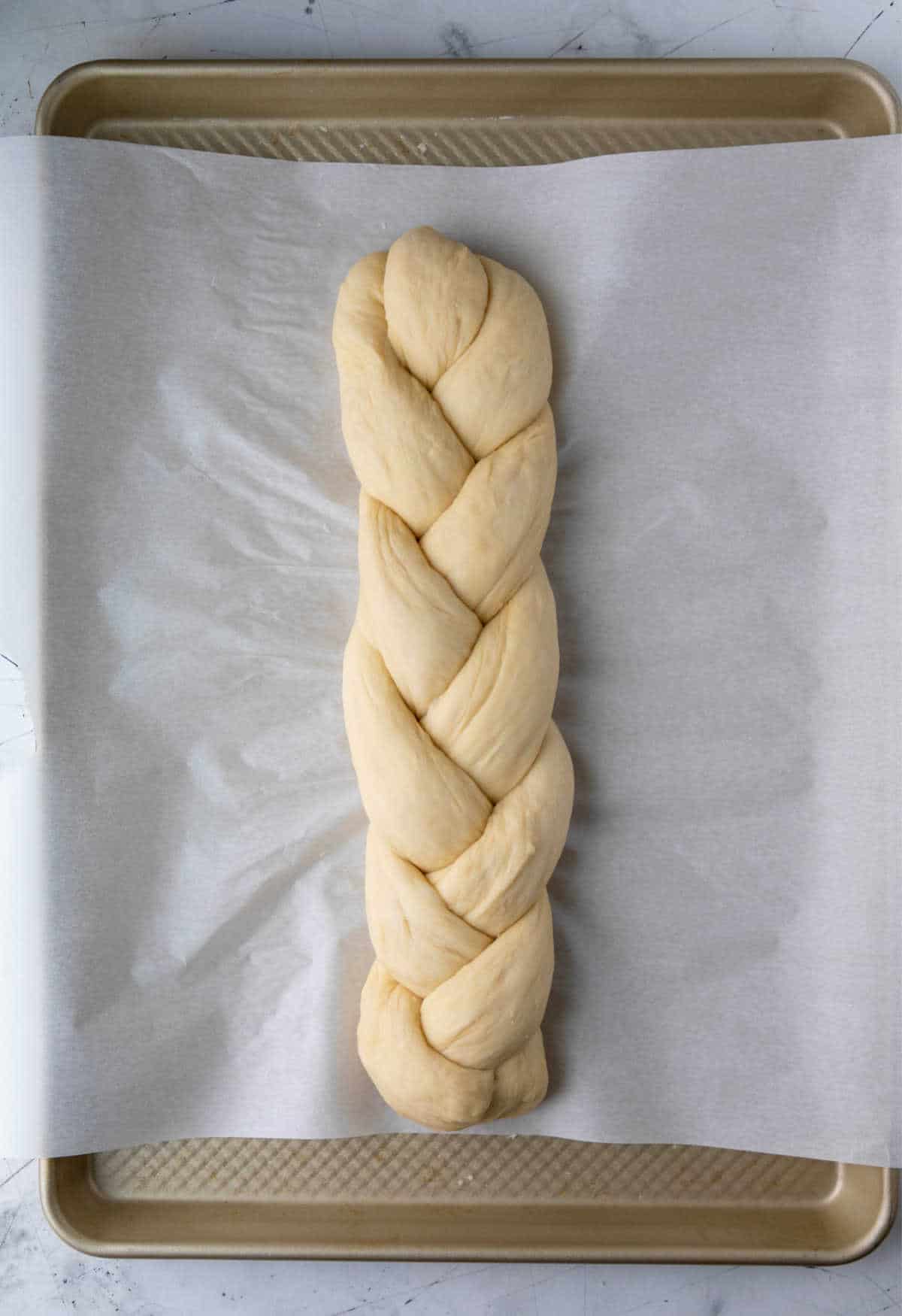 A loaf of unbaked braided bread on a baking sheet. 