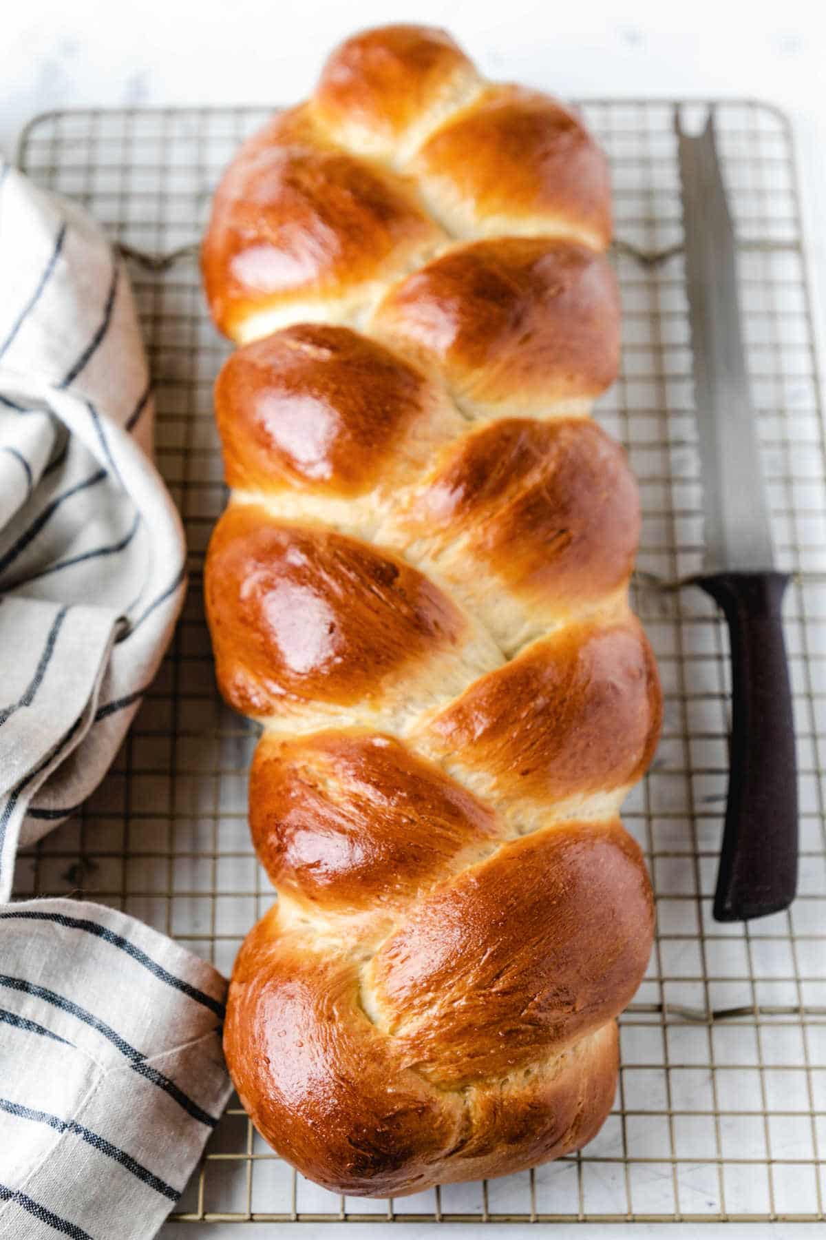 A loaf of braided bread next to a bread knife and a kitchen linen.