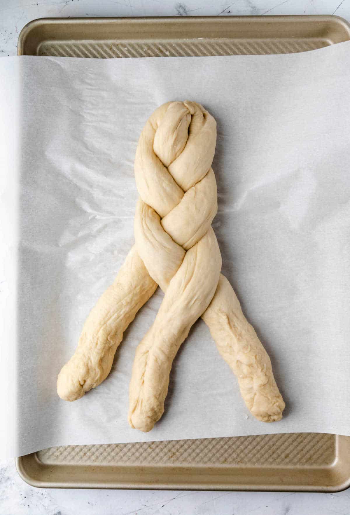 A loaf of partially braided dough on a baking sheet. 