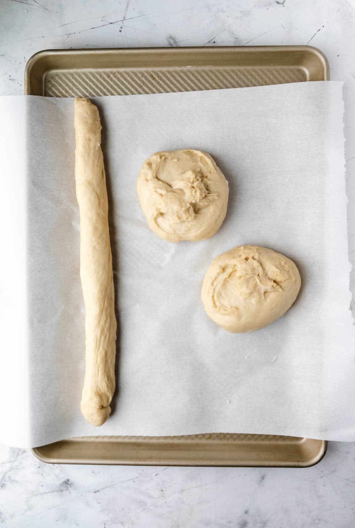 A rope of dough next to two pieces of dough. 