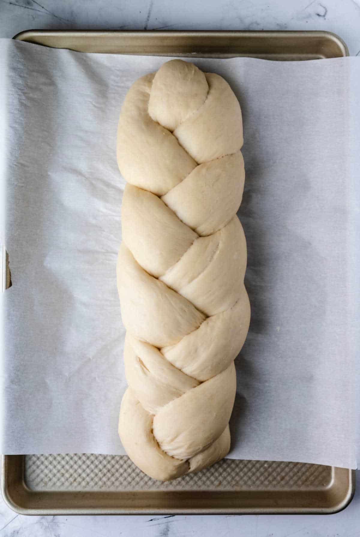 A loaf of risen braided bread on a sheet pan. 