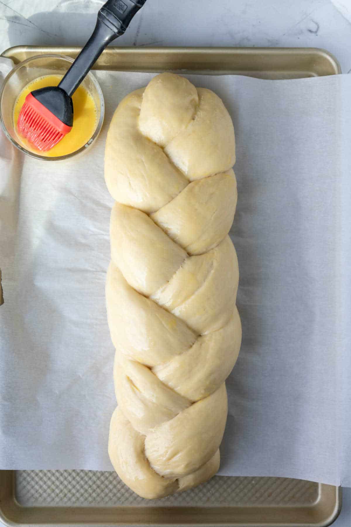 An unbaked loaf of braided bread with egg wash.