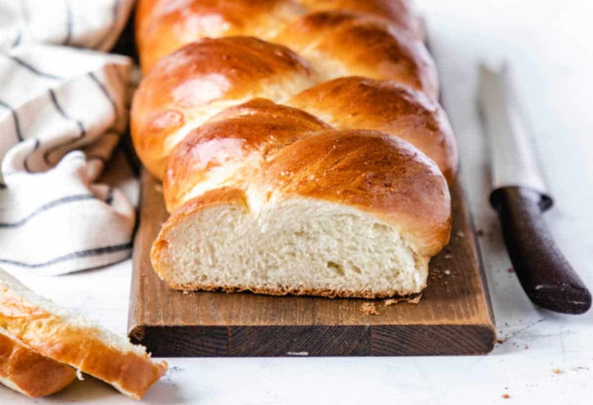 a loaf of braided bread on a cutting board next to a bread knife.