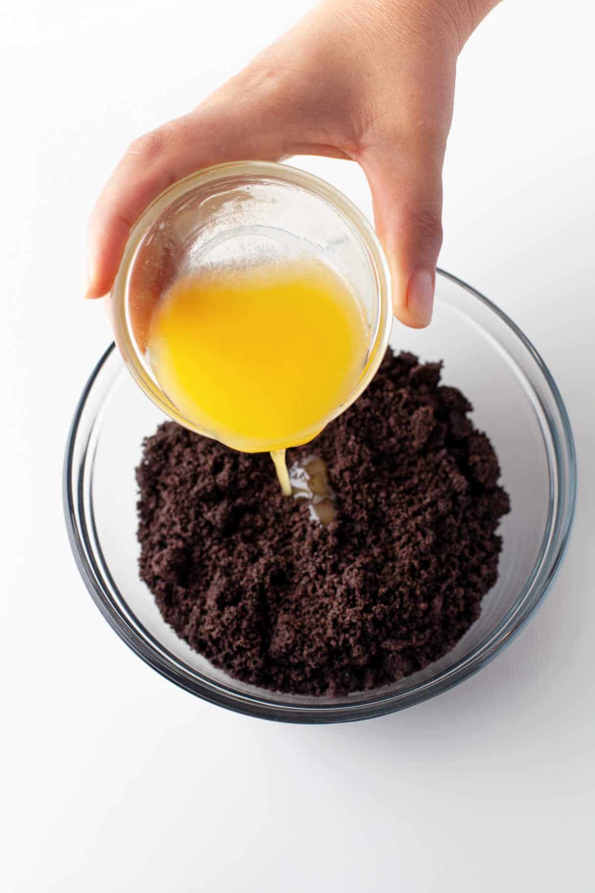 A dish of melted butter pouring into oreo crumbs. 