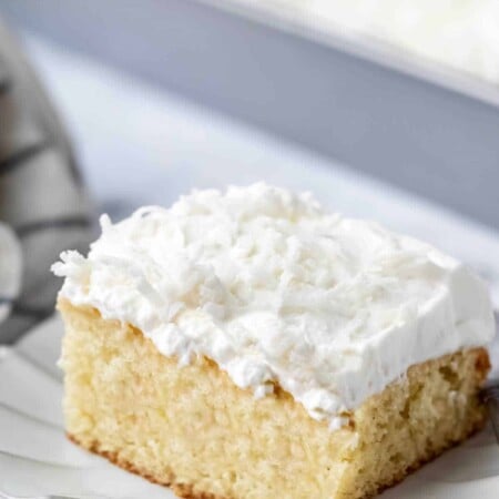 A slice of coconut poke cake on a scalloped plate.