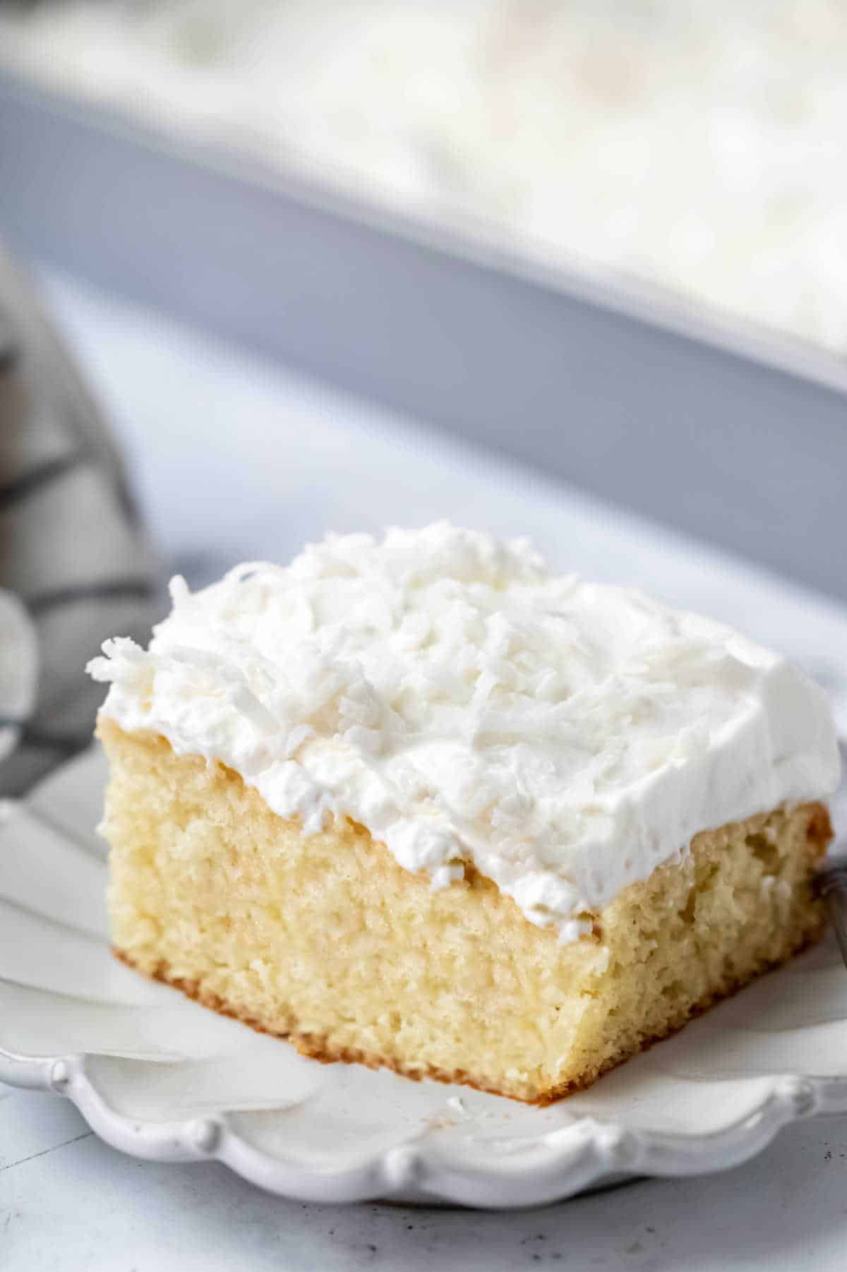 A slice of coconut poke cake on a scalloped plate. 