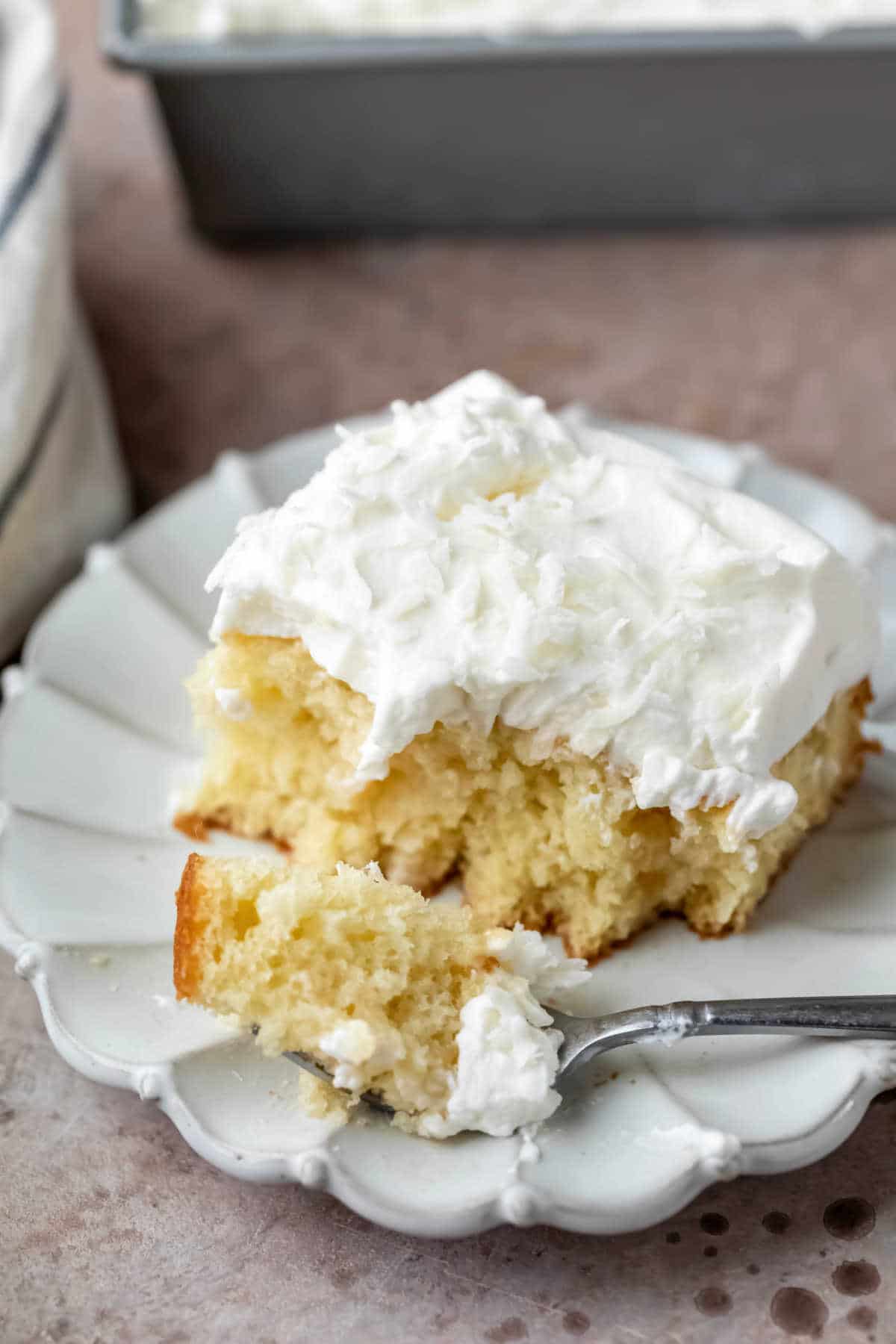 A bite of poke cake next to a piece of coconut poke cake. 