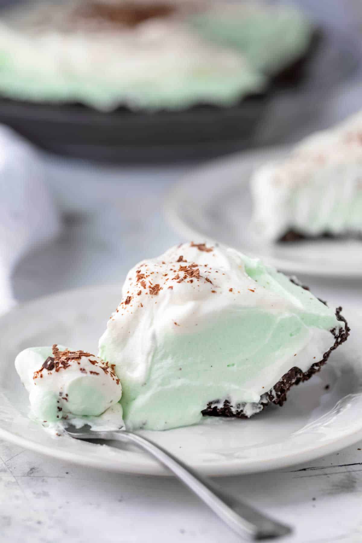 A slice of grasshopper pie on a white plate with a fork taking a bite.