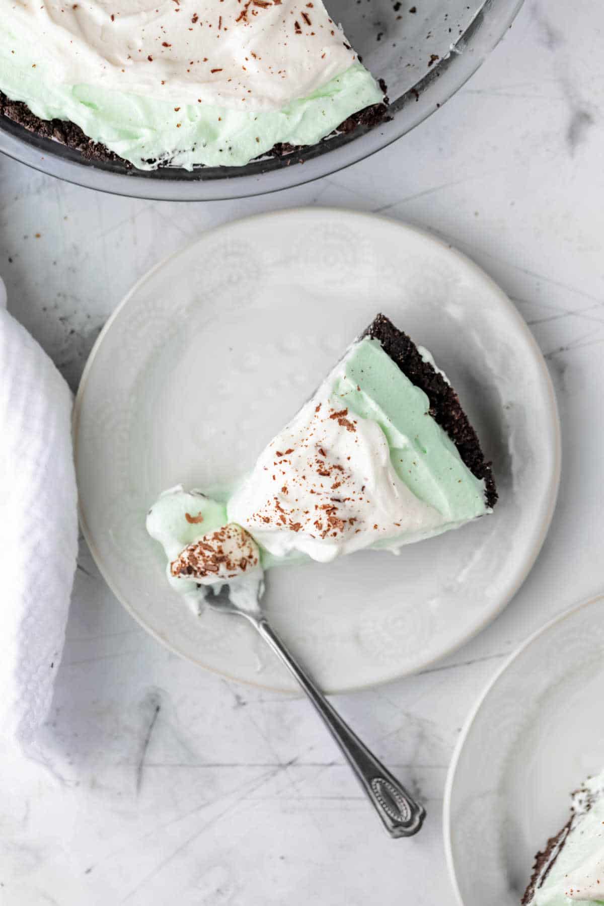 A piece of grasshopper pie on a white plate with a fork in it.