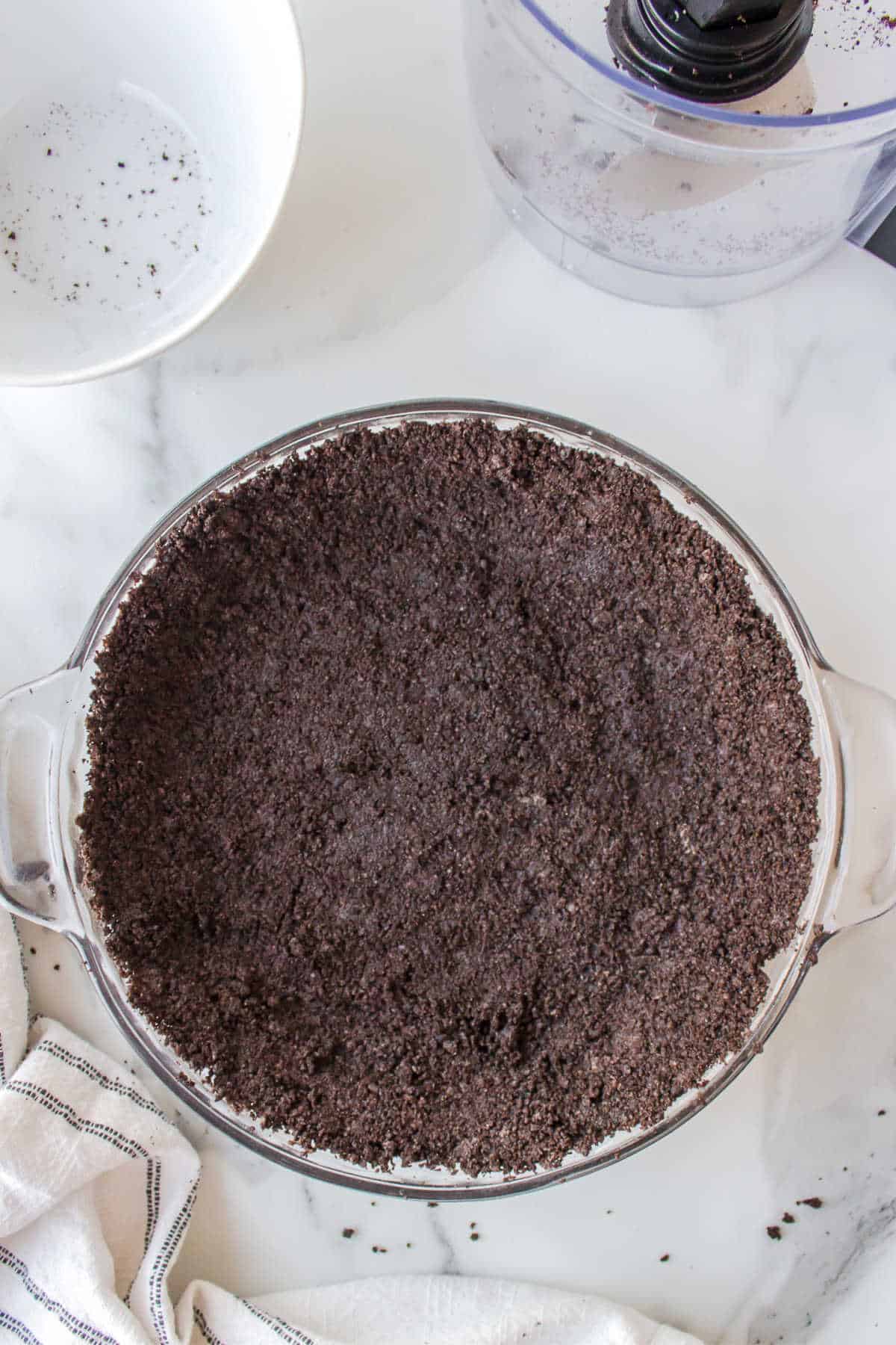 Oreo cookie crust next to an empty food processor.