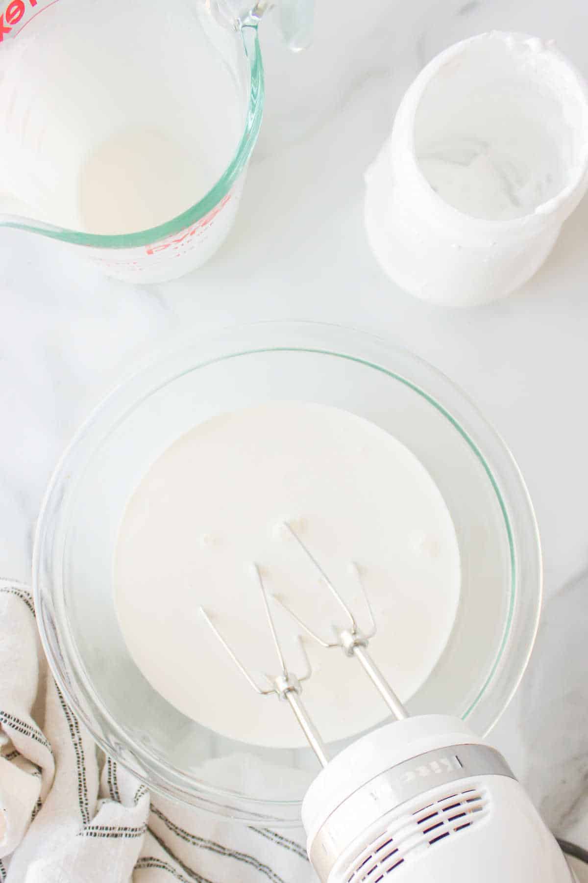 Electric hand mixer beating a bowl of whipped cream.
