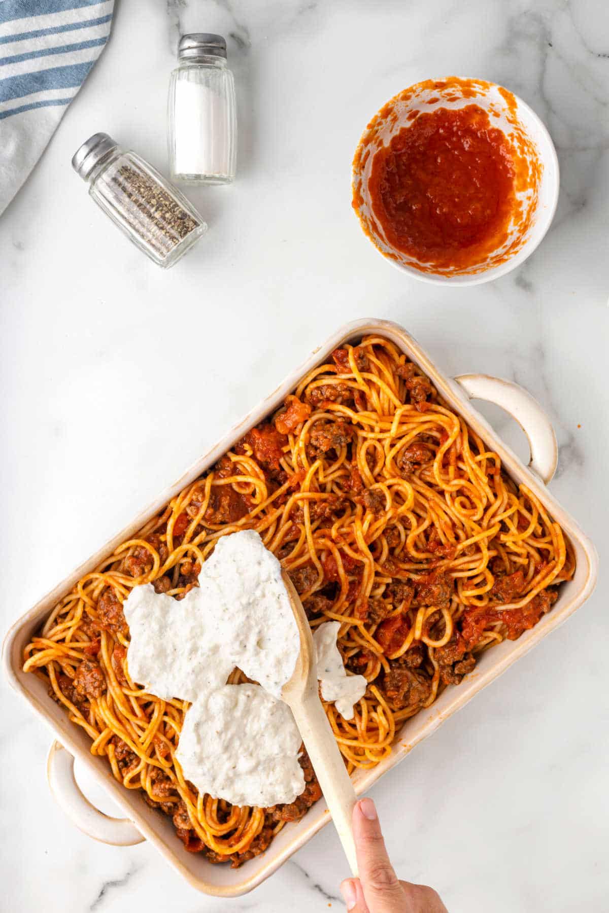 A wooden spoon spreading cheese mixture over spaghetti noodles. 