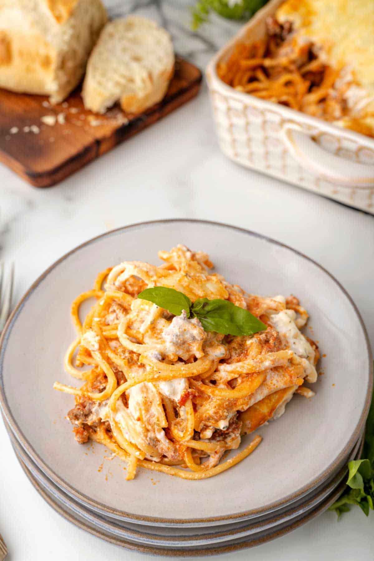 Baked spaghetti on a plate next to a loaf of bread and a casserole pan.