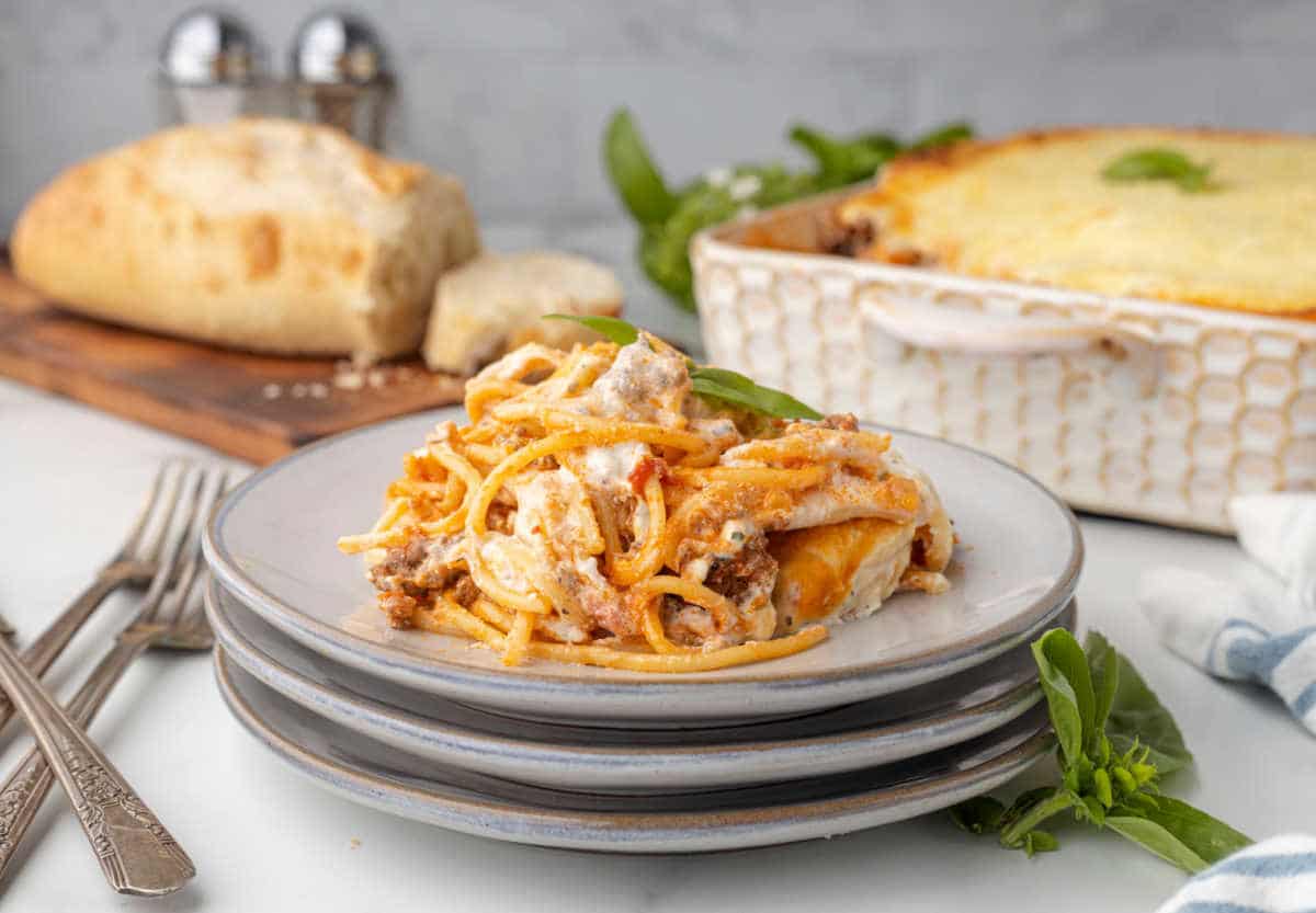 A plate of creamy baked spaghetti on top of two other plates. 