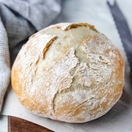 No knead bread on a wooden cutting board next to a bread knife.