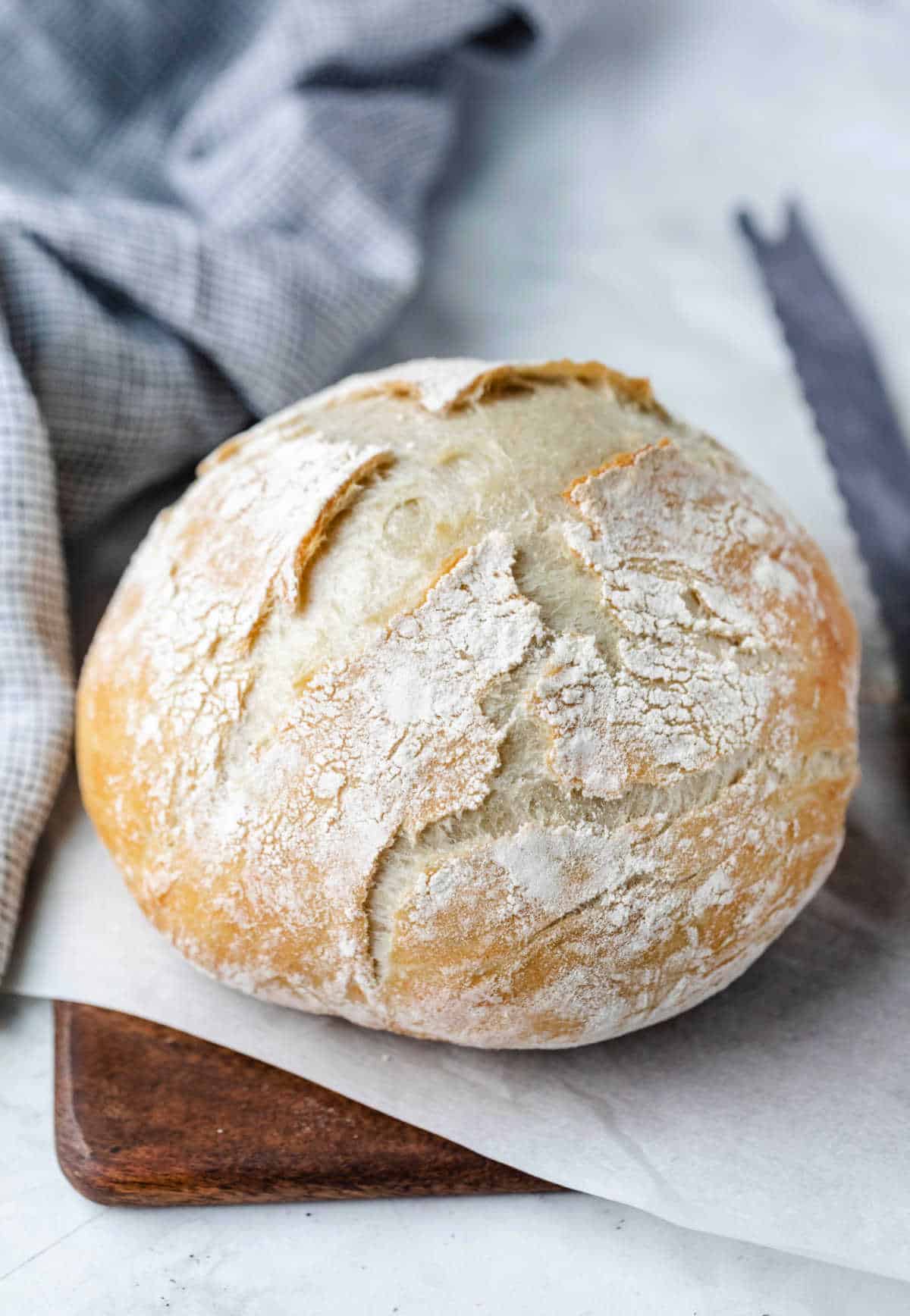 No knead bread on a wooden cutting board next to a bread knife.