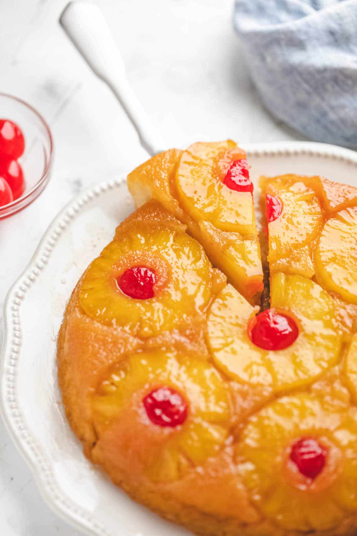 A pineapple upside down cake next to a bowl of maraschino cherries.