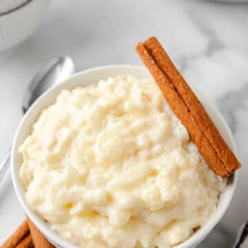 A bowl of rice pudding with a cinnamon stick on the edge of the bowl.