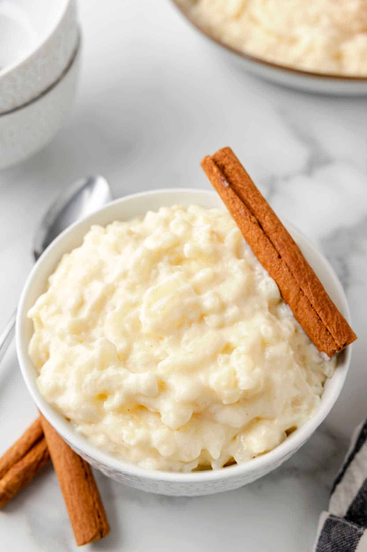 A bowl of rice pudding with a cinnamon stick on the edge of the bowl.