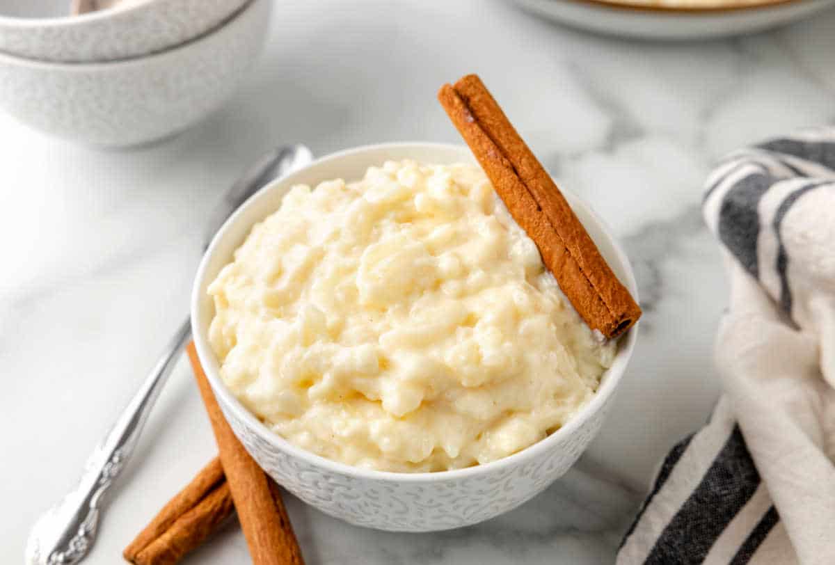 A bowl of rice pudding next to a dish towel and silver spoon.