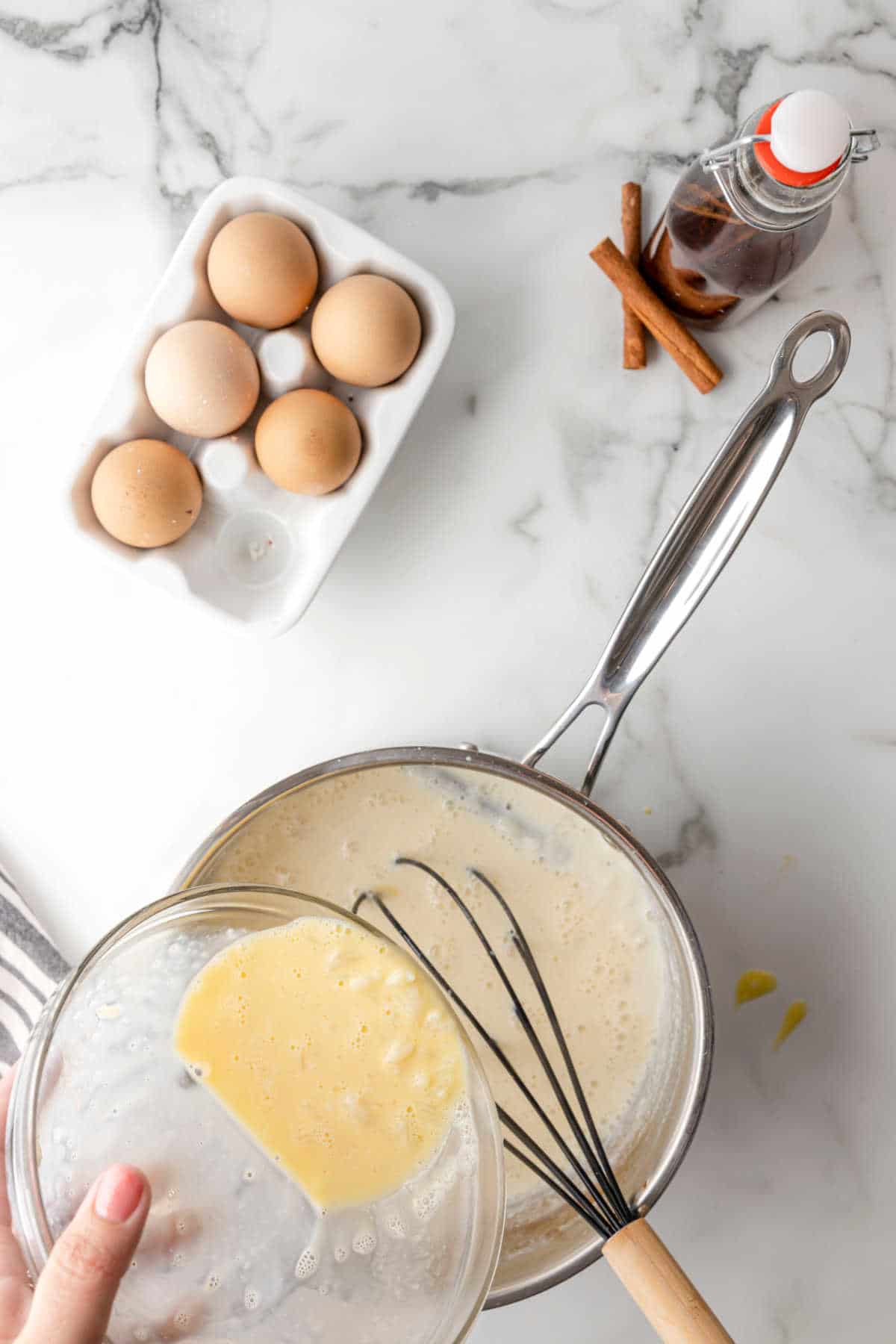 Whisking egg and hot rice pudding into a saucepan.