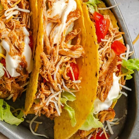 Close up of a shredded chicken taco topped with tomatoes and sour cream.