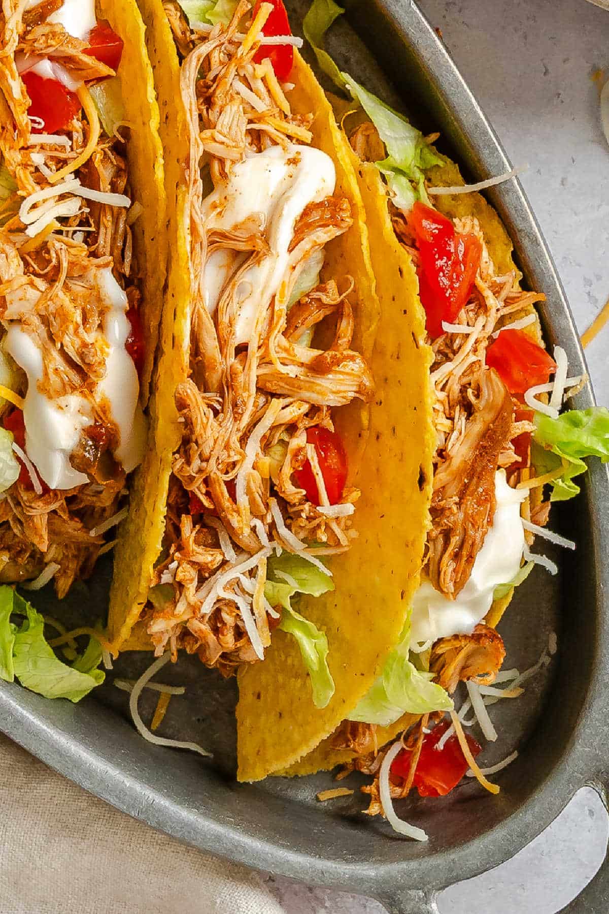 Close up of a shredded chicken taco topped with tomatoes and sour cream.
