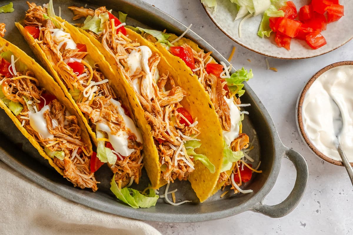 Chicken tacos on a platter next to lettuce, tomatoes, and sour cream. 