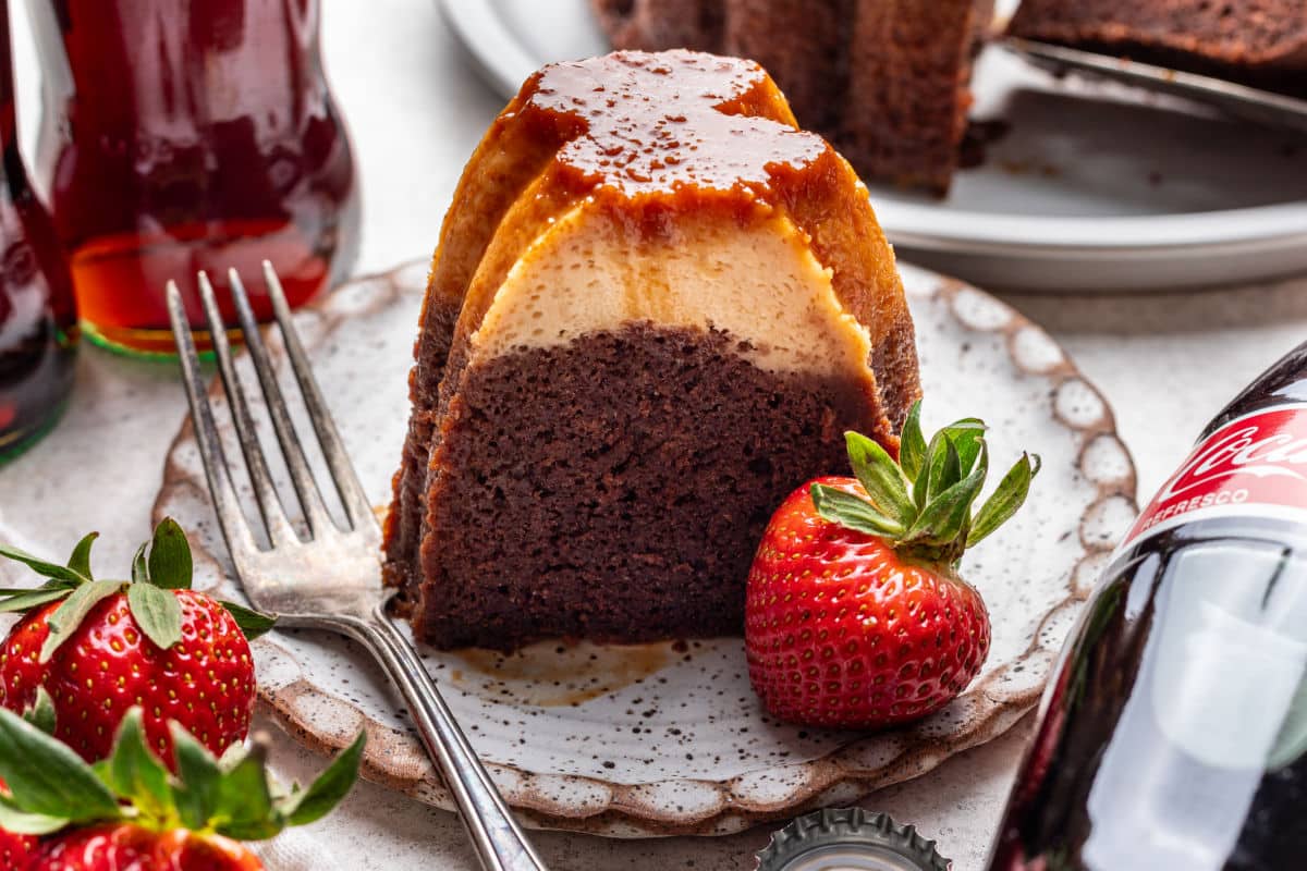 A slice of chocoflan on a plate next to a strawberry and a fork.