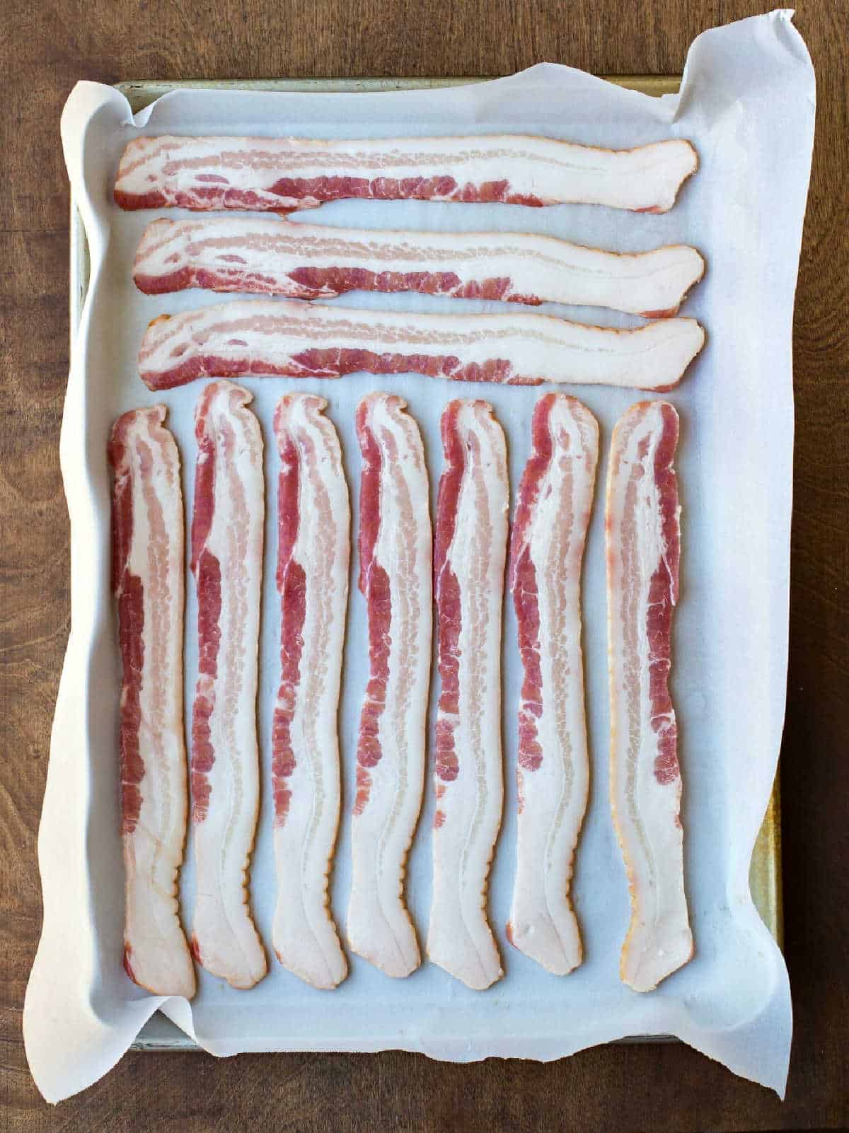 Uncooked bacon on a parchment lined baking tray.